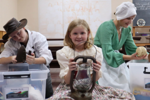 Children in 'olden day' costume, examining historical objects